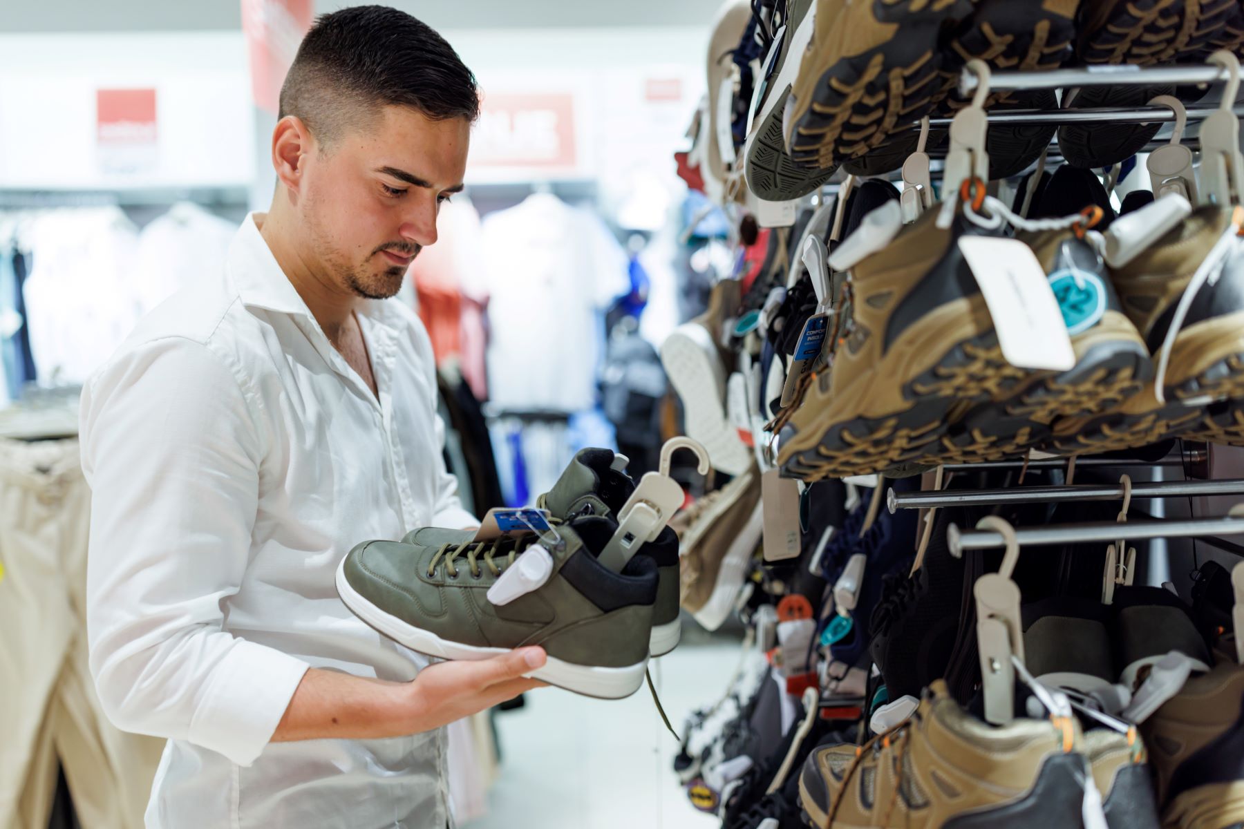 Man in a white shirt examining a green sneaker while standing next to a shoe rack in a store.